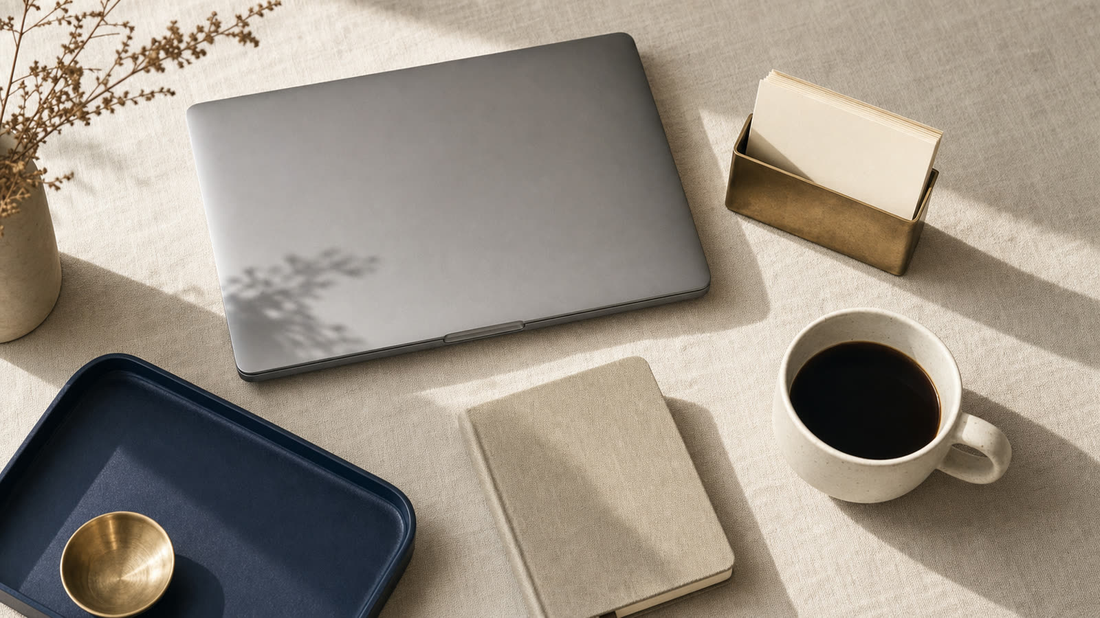 A laptop, leather notebook, and coffee on a warm desk in morning light